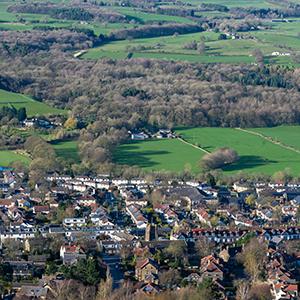 Wide view of a landscape with a town, fields, hedges and woods by Jonny Gios on Unsplash.com